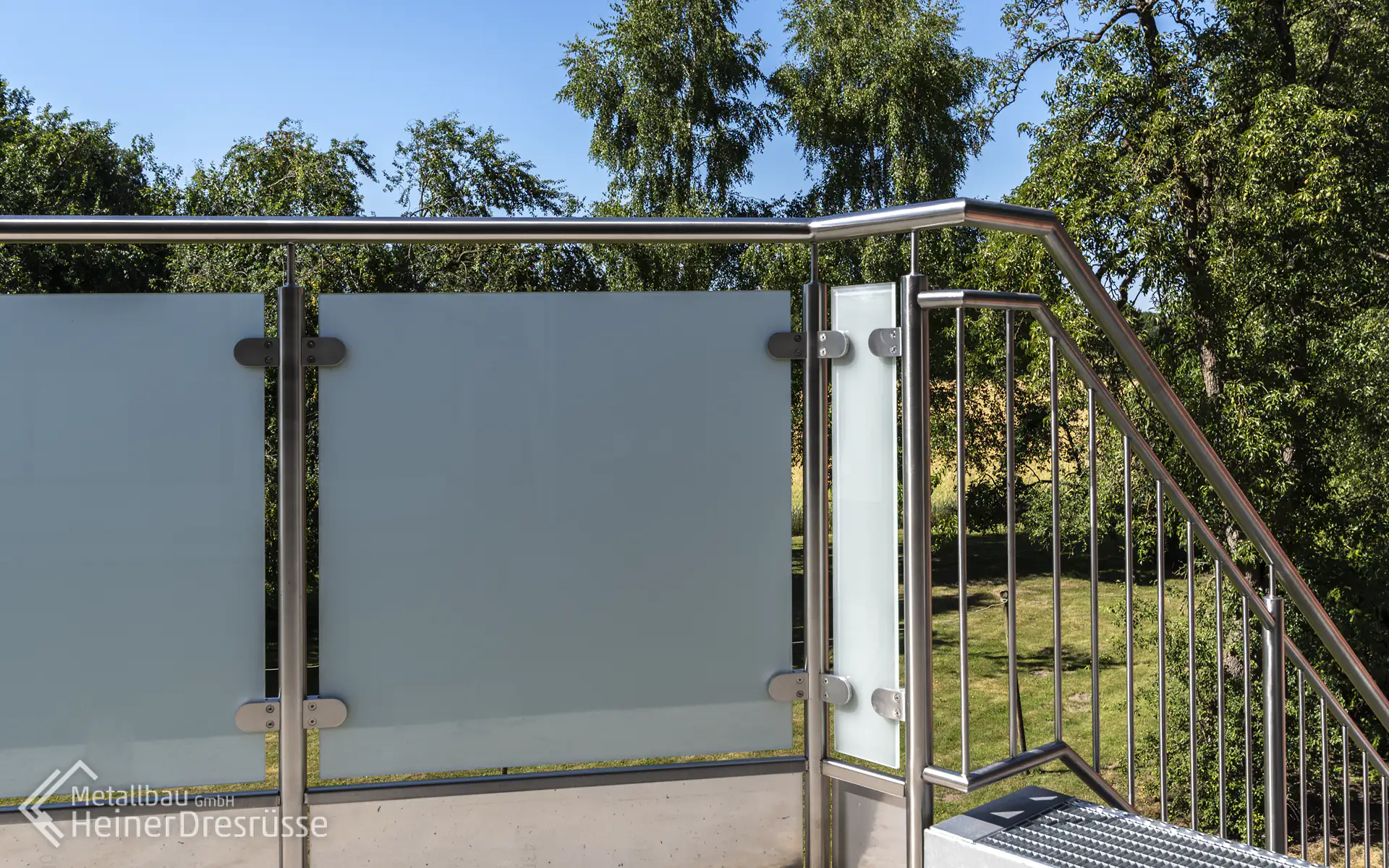Datailaufnahme des Balkongeländers mit Edelstahlhandlauf und Milchglas in Glasklemmhaltern